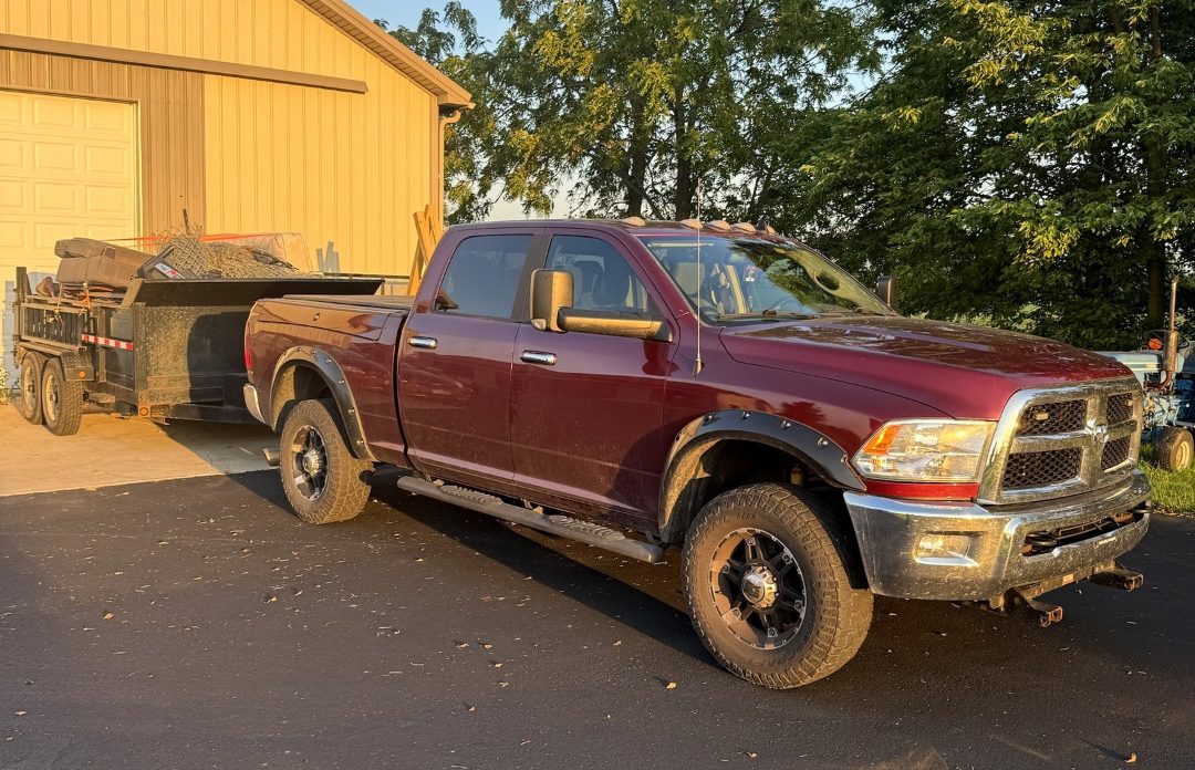 The WorkHorse pickup truck hitched to a loaded black dump trailer in a driveway